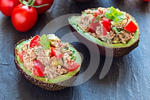 Salad with tuna, avocado, tomatos, coriander and lemon juice served in avocado bowls, ingredients on background, horizontal