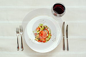 Salad with turkey pepper mushrooms, cornichots and vegetables, in a white plate on a light background, cutlery and red wine, table