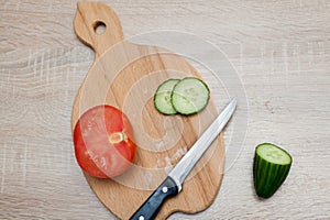 Salad vegetables, chopped cucumbers, a tomato and a kitchen knife lie on a wooden board