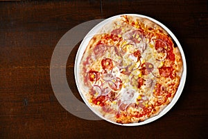 Salami nad sweetcorn pizza on dark brown table from abo