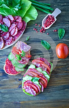 Salami sandwich with tomatoes and cucumbers next sliced salami and tomato and Basil leaves with salad on wooden background