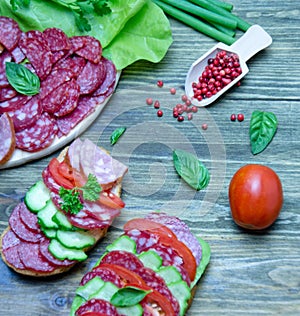 Salami sandwich with tomatoes and cucumbers next sliced salami and tomato and Basil leaves with salad on wooden background