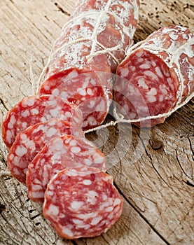 Salami sausages sliced with pepper, garlic and rosemary on cutting board on wooden table.