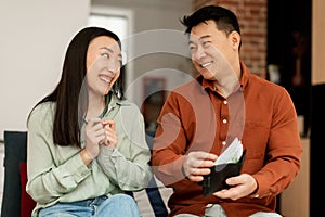 Salary and daily expenses concept. Happy asian man giving money to his wife, woman looking at husband and asking money