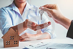 Sale Agent giving house keys to woman customer and sign agreement documents for realty purchase