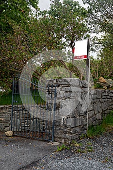 For sale blank sign at a gate of a property on an old stone fence. Real estate business. Mature property on the market to purchase