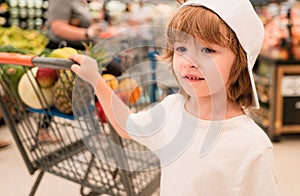Sale, consumerism and people concept - happy little child with food in shopping cart at grocery store.