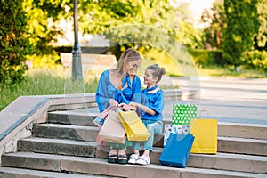 Sale, consumerism and people concept - happy young women her dauther with shopping bags walking city street