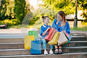 Sale, consumerism and people concept - happy young women her dauther with shopping bags walking city street