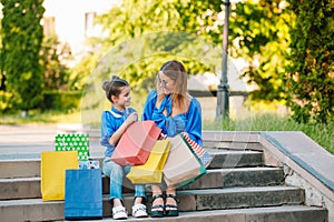 Sale, consumerism and people concept - happy young women her dauther with shopping bags walking city street