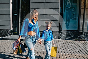 sale, consumerism and people concept - happy young women her dauther with shopping bags walking city street