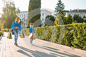 sale, consumerism and people concept - happy young women her dauther with shopping bags walking city street