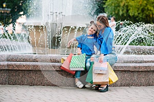 sale, consumerism and people concept - happy young women her dauther with shopping bags walking city street