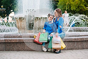 sale, consumerism and people concept - happy young women her dauther with shopping bags walking city street