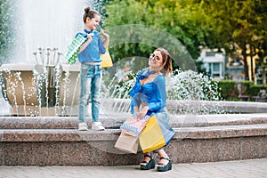 Sale, consumerism and people concept - happy young women her dauther with shopping bags walking city street