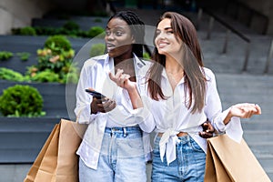 Sale, consumerism and people concept. Happy young women looking into shopping bags at in city