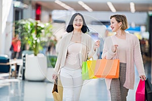 Sale, consumerism and people concept - happy young women with shopping bags walking and smiling in mall