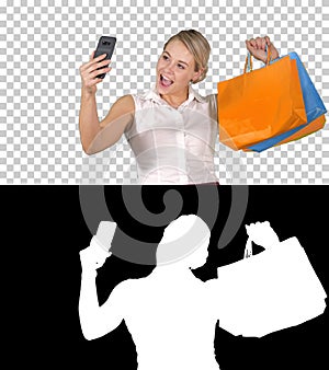 Sale, consumerism, technology and people concept - happy young woman with smartphone and shopping bags taking selfie