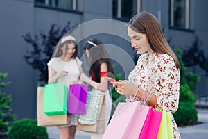 Sale, consumerism, technology and people concept - happy young women with smartphones and shopping bags.