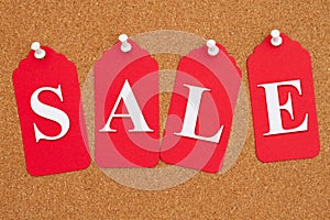 Sale message on red gift tags on a corkboard