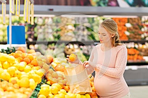 Pregnant woman with bag buying oranges at grocery