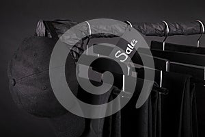 Sale sign. Black cap and pant, jeans hanging on clothes rack background. friday. Close up.