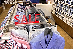 Sale sign in the department of men`s shirts and jackets in the store. Colorful clothes on hangers in a retail shop. Season sale,
