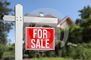 Sale sign near beautiful house outdoors. Red signboard with words