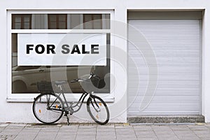 For sale sign in store window with bicycle parked outside - shop vacancy