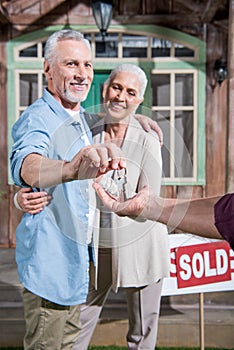 Saleman giving keys of new house to happy senior couple photo