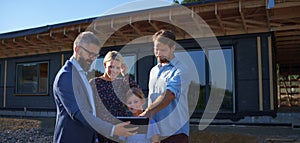 Sales Agent showing plans of new house to young family on construction site.