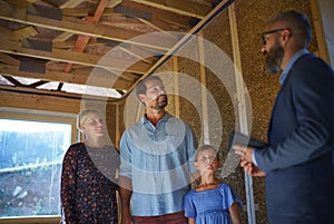 Sales Agent showing plans of new house to young family on construction site.