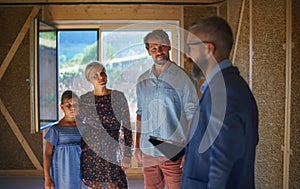 Sales agent showing plans of new house to young family on construction site.