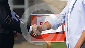 Sales agent and young man shaking hands on sold sign background, agency service