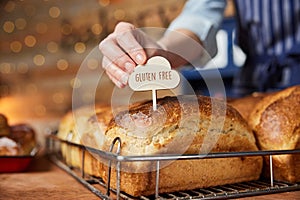 Sales Assistant In Bakery Putting Gluten Free Label Into Freshly Baked Baked Sourdough Loaves Of Bread