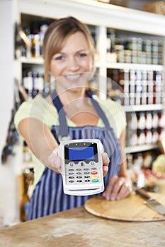 Sales Assistant In Food Store Handing Credit Card Machine To Customer