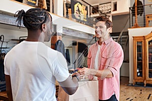 Sales Assistant Handing Purchases To Male Customer In Fashion Store