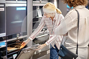Sales assistant in striped shirt showing new ovens to the customer