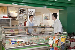 Sales Clerk smiling and assisting man at the Deli counter in supermarket