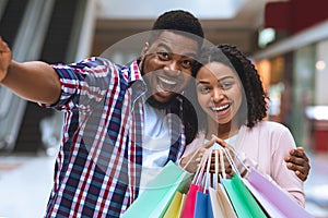 Sales And Consumerism. Excited Black Couple Taking Selfie While Shopping In Mall