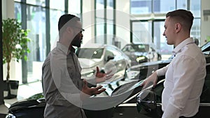 Sales manager car talk to african man customer and explain vehicle detail with gesture. Guy