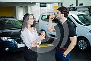 Sales manager describing car to customer in showroom while drinking coffee