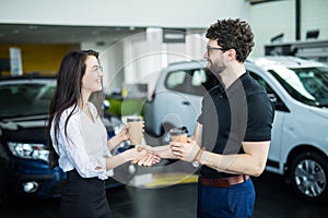 Sales manager describing car to customer in showroom while drinking coffee