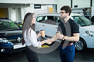 Sales manager describing car to customer in showroom while drinking coffee