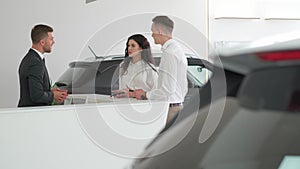 Sales manager helping young couple to choose a new car in modern car showroom.