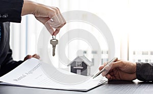 Sales manager or real estate agent holds the key handing it to the customer after signing the house purchase contract with home in