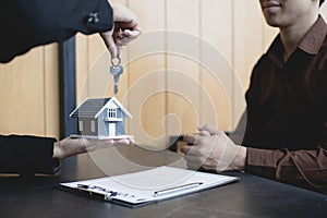 Sales manager or real estate agent holds the key handing it to the customer after signing the house purchase contract with home in