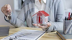 Sales manager or salesperson holds a demo house and has a home purchase contract with keys to deliver to customer buys a house