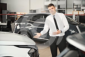 Sales manager standing in car showroom presenting new model of automobile