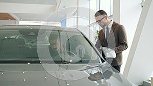 Sales manager talking to client sitting in car in showroom choosing automobile